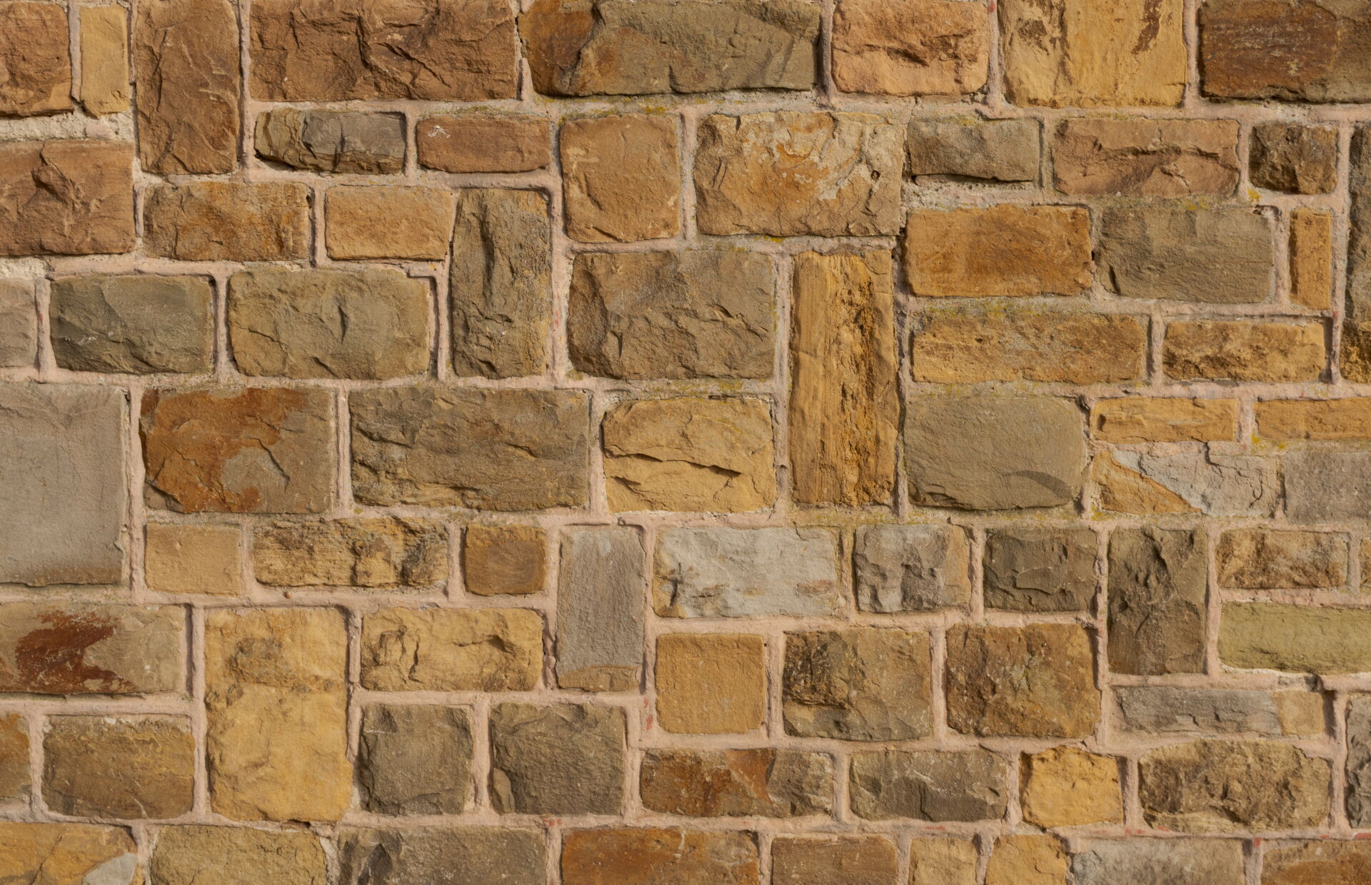 Eine detailreiche Aufnahme einer unregelmäßigen Natursteinmauer in verschiedenen Braun- und Beigetönen. Mögliche Gestaltungsidee vom Fliesenfachbetrieb Behnisch GmbH.