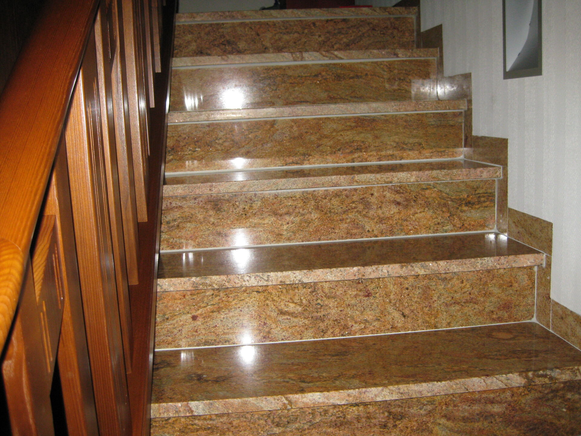 Eine polierte Granittreppe in warmen Braun- und Beigetönen mit Holzgeländer, verlegt vom Fliesenfachbetrieb Behnisch GmbH in Pulsnitz.