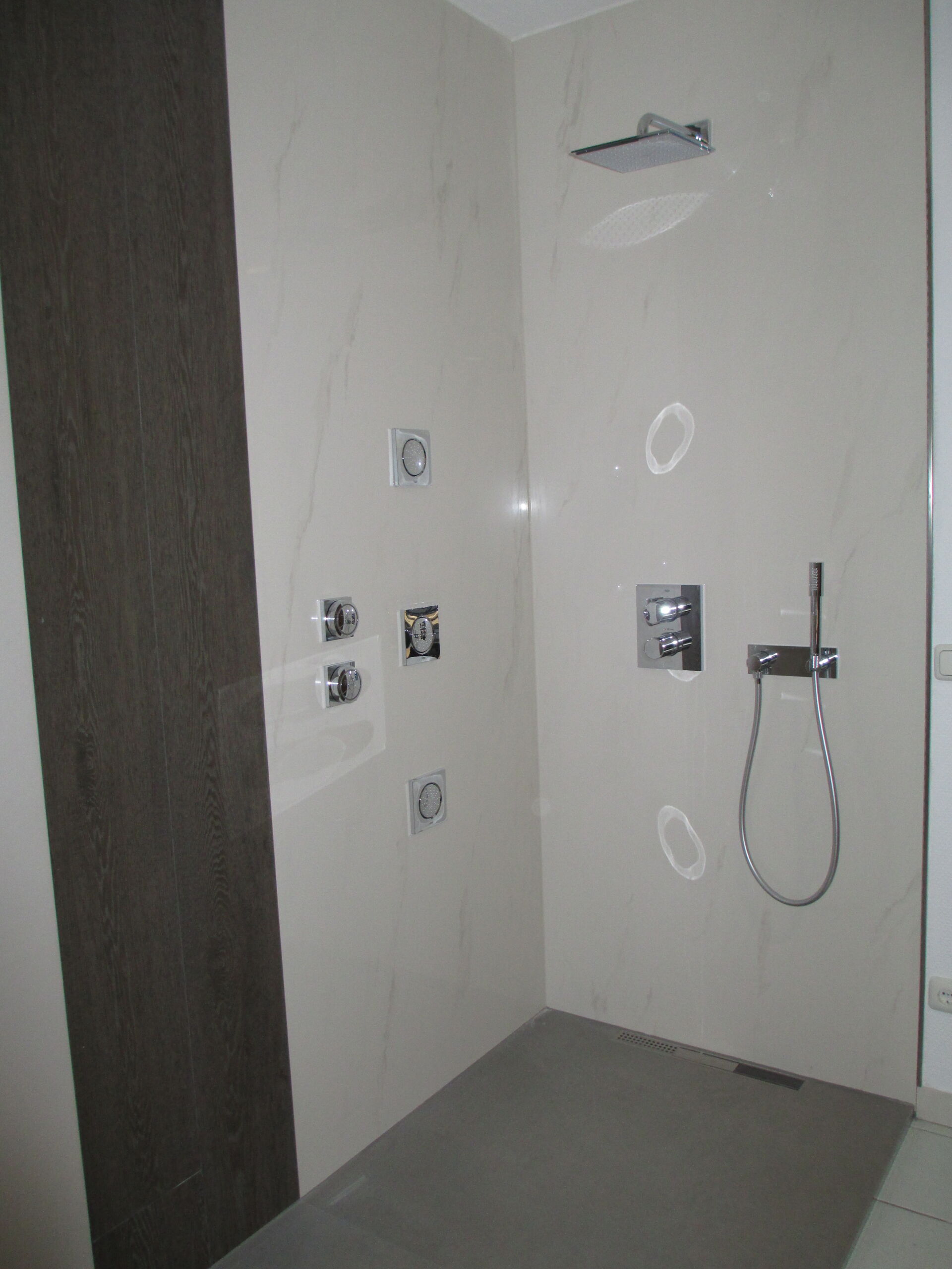 Eine barrierefreie Dusche mit hellen Wandfliesen, dunkler Akzentwand und grauem Boden, gestaltet vom Fliesenfachbetrieb Behnisch GmbH in Pulsnitz.